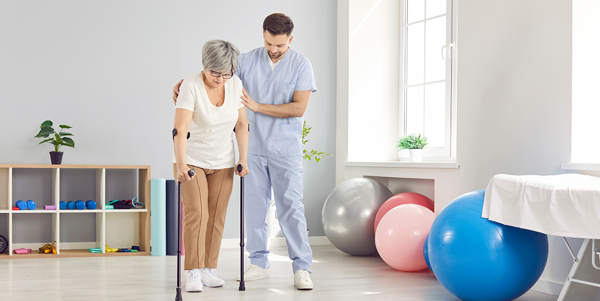 A rehabilitation specialist at a clinic helps an elderly woman walk on crutches
